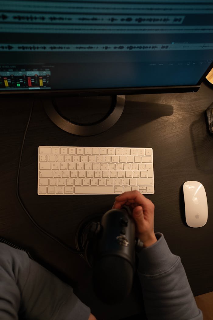 services-03 A detailed view of a person using a microphone and computer setup in a recording studio.